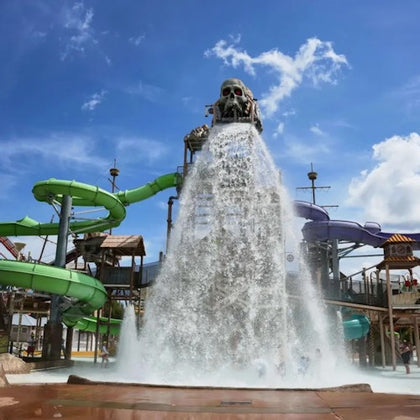 A large water park play area featuring a pirate-themed bucket dumping water and green and purple slides under a blue sky.