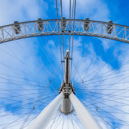 View from below of a giant Ferris wheel structure against a blue sky with scattered clouds.