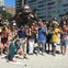 A group of people posing in front of bronze laughing statues in an outdoor urban area on a sunny day.