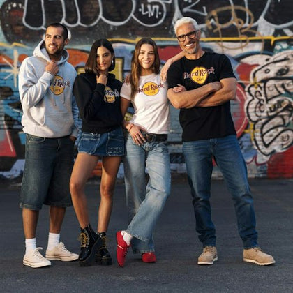 Four people in Hard Rock Cafe clothing pose in front of a wall with colorful graffiti.