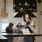 Two people observe exhibits in a music-themed room, featuring a guitar on the wall and a large artwork of a musician.