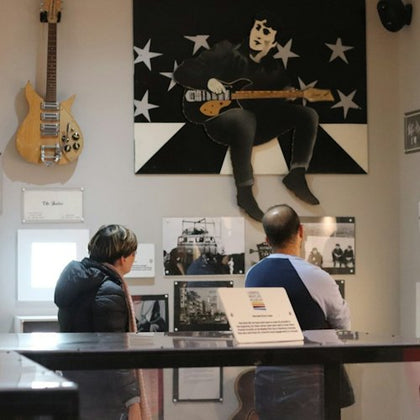 Two people observe exhibits in a music-themed room, featuring a guitar on the wall and a large artwork of a musician.