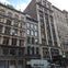 A row of historic urban buildings with ornate facades, a parked truck, and a cloudy sky in the background.