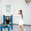 Two people pose with a large chair illusion, one sitting on it, the other pointing at the Museum of Illusions Denver sign.