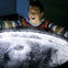 A smiling child interacts with a circular display emitting light and mist, wearing a colorful striped sweater.
