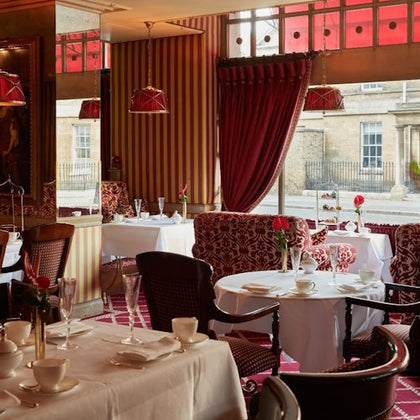 Elegant restaurant interior with red and gold decor, white tablecloths, and windows overlooking a street.