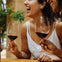 Two people smiling and holding wine glasses with red wine, seated at a wooden table, with plants in the background.