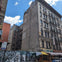 A city street with an old multi-story building, graffiti-covered walls, and a shop with a yellow awning under a blue sky.
