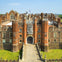 Aerial view of a large, historic brick building with multiple chimneys and towers, featuring a gated central entrance.