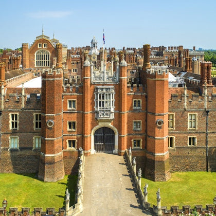 Aerial view of a large, historic brick building with multiple chimneys and towers, featuring a gated central entrance.
