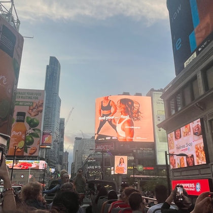 Open top double decker tour bus approaching Yonge-Dundas Square. Multiple billboard and TV screens showing advertising. 