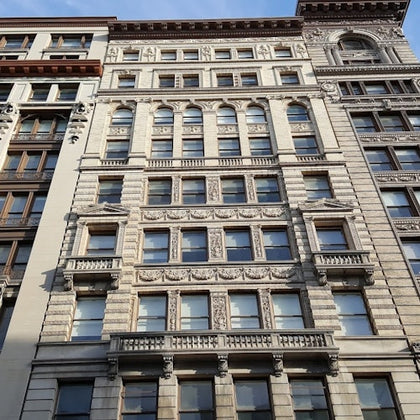 A multi-story historic building facade with ornate details, arched windows, and decorative stone carvings under a blue sky.