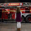 A girl stands in front of a damaged fire truck labeled 'Ladder 3' displayed in a museum setting.