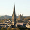 A scenic view of a city with prominent church spires and rooftops, surrounded by trees and hills under a clear sky.