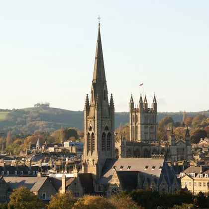 A scenic view of a city with prominent church spires and rooftops, surrounded by trees and hills under a clear sky.