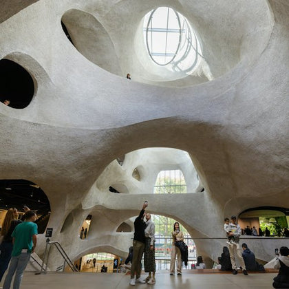 People inside a spacious, modern building with curving white walls and large windows letting in natural light.
