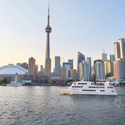 A city skyline with a prominent tower and several buildings by the waterfront, with boats on the water in the foreground.
