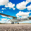 A small propeller plane with registration number N1192M is parked on a runway under a bright blue sky with scattered clouds.