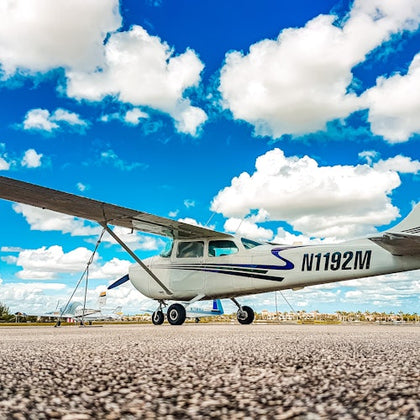 A small propeller plane with registration number N1192M is parked on a runway under a bright blue sky with scattered clouds.