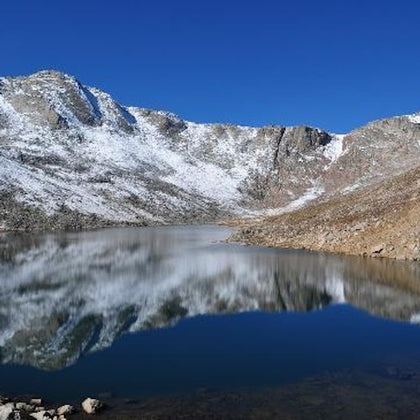 A tranquil mountain lake reflecting snow-covered peaks under a clear blue sky.