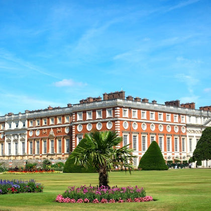 A large, ornate building with red and white exterior sits behind a well-manicured garden with colorful flowers and trimmed hedges.