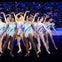 A group of dancers in sparkly costumes performing on a stage with a backdrop of a snowy, starry scene.