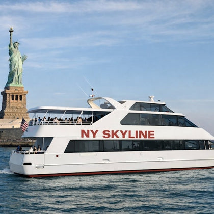 A white tour boat labeled 'NY SKYLINE' on water near the Statue of Liberty under a blue sky.