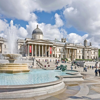 A grand neoclassical building with columns and a dome, surrounded by a square with fountains and visitors walking.