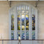 A person walks past a large, colorful stained glass window depicting a natural landscape inside a building.