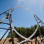 A roller coaster with blue and green tracks, carrying passengers, moving on a wooden frame structure, surrounded by greenery.