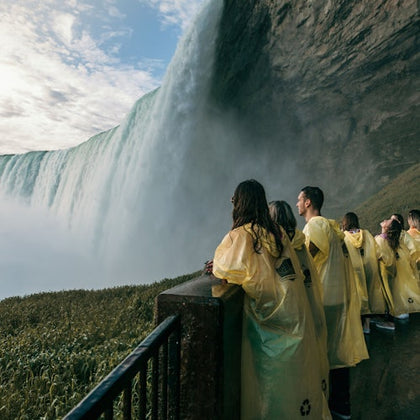 People in yellow rain ponchos stand near a railing, observing a large waterfall cascading from a cliff.
