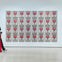 A gallery wall displaying 32 framed artworks of Campbell's soup cans in rows. A person in red walks by on the left.