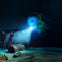 Three people wearing VR headsets stand on an ocean floor with a glowing underwater robotic craft and sunken artifacts around them.