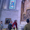 People observing an ornate religious display inside a cathedral, with stained glass and paintings visible in the background.