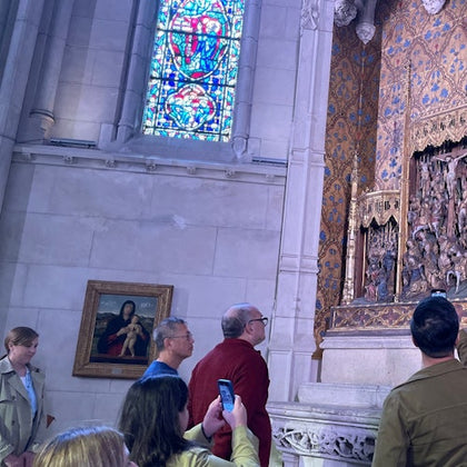 People observing an ornate religious display inside a cathedral, with stained glass and paintings visible in the background.