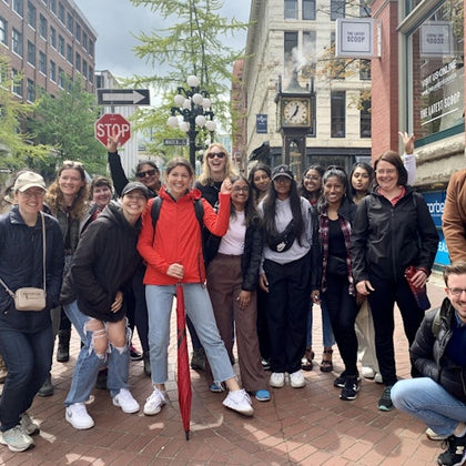 A group of people posing for a photo on a cobblestone street near a steam clock and a stop sign in an urban area.
