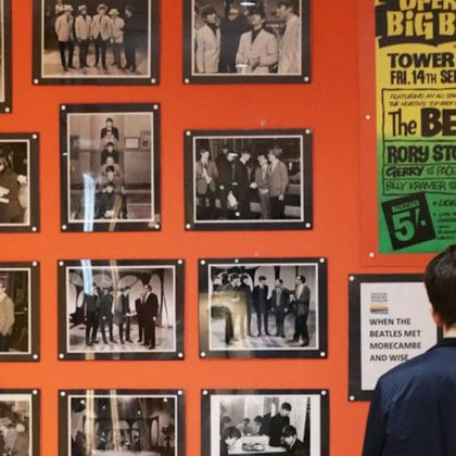 A museum display featuring black-and-white photos of The Beatles, with a person viewing the exhibit.