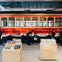 People interacting with exhibits in a museum featuring a red vintage streetcar and wooden display tables with items.
