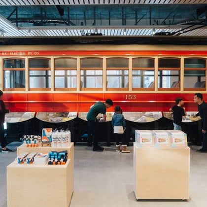 People interacting with exhibits in a museum featuring a red vintage streetcar and wooden display tables with items.