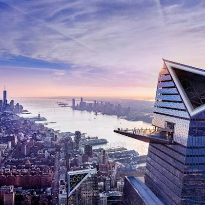 Skyscraper with an outdoor observation deck overlooking a cityscape at sunset, with a river and skyline in the background.