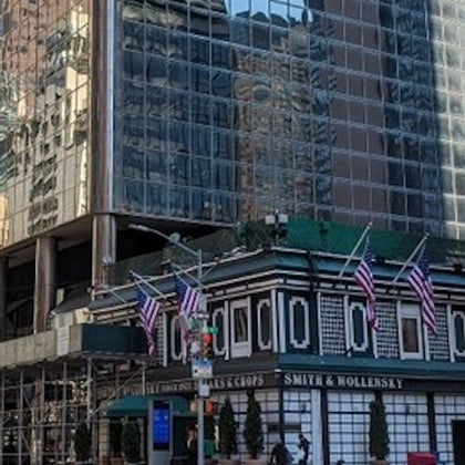 A city building with a restaurant at the base displaying American flags and surrounded by reflective glass structures.