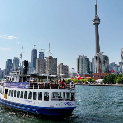 A sightseeing boat named 'Oriole' on water with the CN Tower and Toronto skyline in the background under a clear sky.