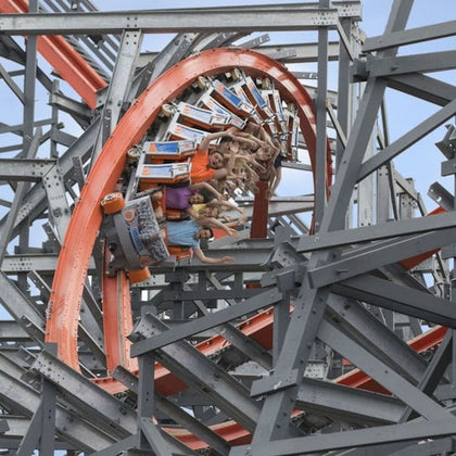 People riding a rollercoaster with an orange loop and a grey steel frame structure, appearing upside down in the loop.
