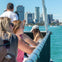 People on a boat enjoying the view of a city skyline in the background on a sunny day.