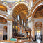 Interior of a grand cathedral with ornate arches, detailed frescoes, and a central altar with lit candles.