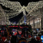 A festive street at night with illuminated angel decorations, viewed from a bus with passengers wearing Santa hats.