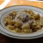 A plate of rigatoni pasta with creamy sauce, bacon bits, and grated cheese, served on a wooden table.