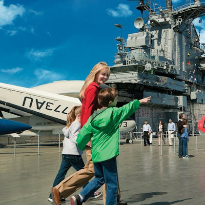 Children walking and pointing on the deck of the Intrepid Sea, Air & Space Museum, with aircraft and the ship's structure visible.