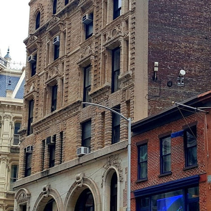 A street view of a brick building with arched windows, neighboring structures, and a lamppost in front.