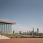 Modern building with glass facade on the left, steps and a person walking down. City skyline visible in the background.